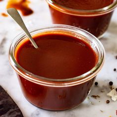 two jars filled with sauce sitting on top of a white counter next to a knife