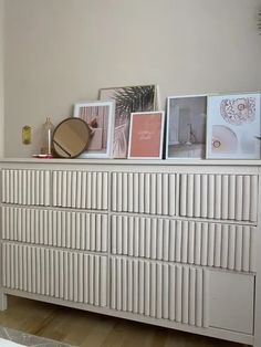 a white dresser topped with pictures and framed art on top of it's drawers