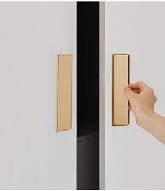 a hand is holding the door handle on a white cabinet with black and gold trim