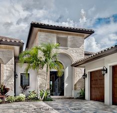 a house with two garages and palm trees in front of it on a cloudy day