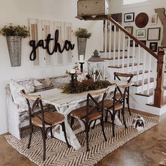 a dining room table and chairs in front of a stair case with letters on the wall