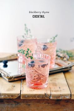 three glasses filled with blueberries and mint sprigs on top of a wooden tray