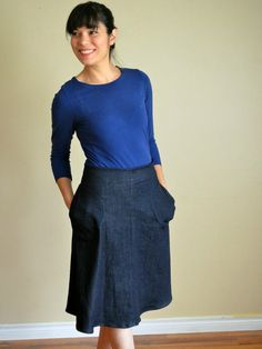 a woman standing in front of a wall wearing a blue shirt and black denim skirt