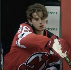 a young man holding a hockey stick in his hand and wearing a red jersey with white lettering on it