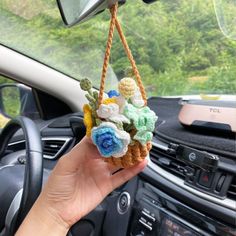 a person holding up a small basket with flowers on it in their hand while sitting in the driver's seat of a car