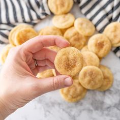 a hand holding a sugary pastry in front of some other pastries on a marble surface