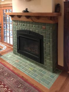 a fireplace in a living room with green tile and wood trimming on the mantle