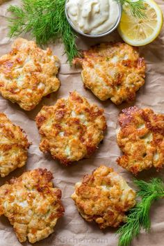 crab cakes with sour cream and dill sprigs on parchment paper next to lemon wedges