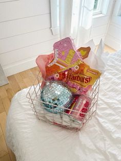 a basket filled with candy sitting on top of a white bed next to a window