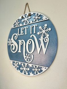 a sign that says let it snow hanging from the side of a wall with snowflakes on it