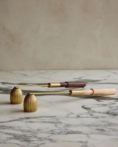 three wooden objects sitting on top of a marble table next to each other, one with a long stick sticking out of it's end