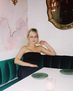 a woman sitting at a table in front of a wall with a mirror on it