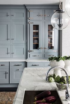 a kitchen with gray cabinets and marble counter tops, an island sink and large glass globe lights