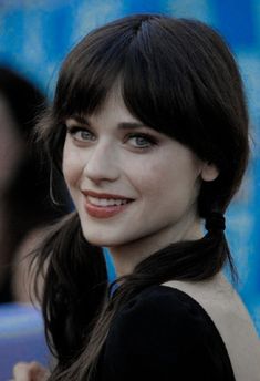 a close up of a person wearing a black dress and smiling at the camera with her hair in a pony tail