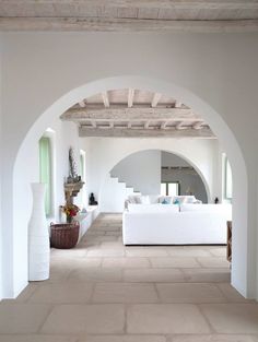 an open living room with white couches and arches on the ceiling, along with potted plants