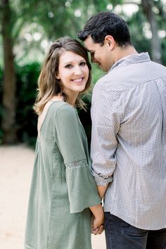 a man and woman holding hands while standing next to each other in front of trees