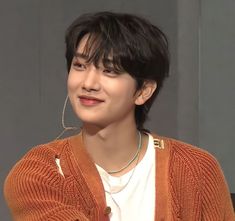 the young man is wearing an orange cardigan and white t - shirt while sitting down