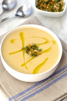 a white bowl filled with soup next to two spoons on top of a table