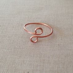 a copper wire ring sitting on top of a beige fabric covered surface, with the letter c in the middle