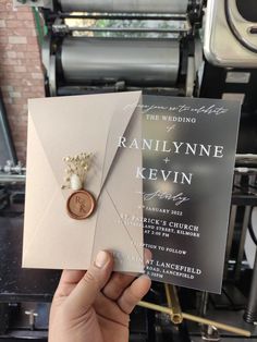 a person holding up a wedding card with a button on it