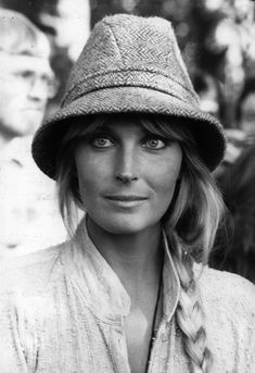 black and white photo of woman wearing hat with man in background behind her looking at camera