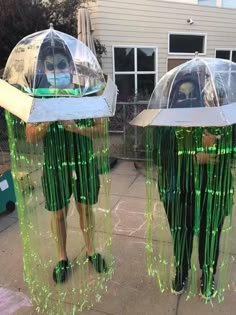 two people wearing green and white costumes standing in front of a building with plastic coverings over their heads