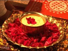 a bowl filled with dip surrounded by red petals on top of a gold platter