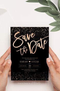 two hands holding up a black and gold save the date card with glitter on it