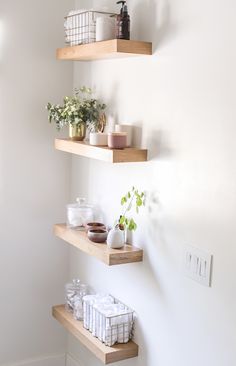 three wooden shelves with plants and other items on them in a white walled bathroom area