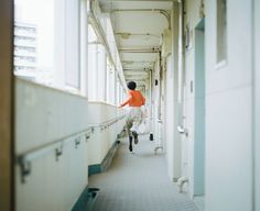 a man in an orange shirt is walking down a long hallway with white walls and windows