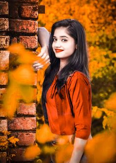 a woman standing next to a brick wall with yellow leaves on it and her hair blowing in the wind