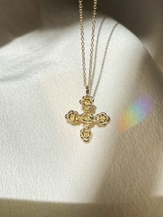 a gold cross necklace on a white cloth with sunlight shining through the window behind it