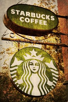 two starbucks signs hanging from the side of a brick building with trees in the background