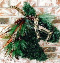 a fake horse head is decorated with pine cones and ribbons for the holiday season, against a brick wall