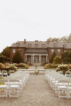 an outdoor ceremony setup with white chairs and flowers in front of a large brick building