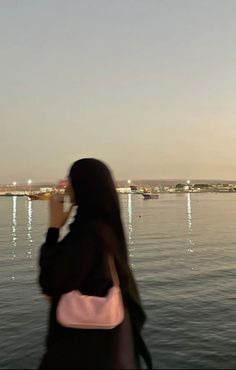 a woman standing in front of the water while looking at her cell phone