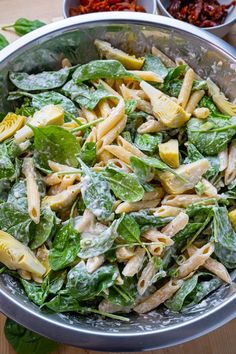 a bowl filled with pasta and spinach on top of a wooden table next to other dishes