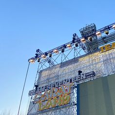 an outdoor concert stage with lights and signs on it's sides, in front of a clear blue sky