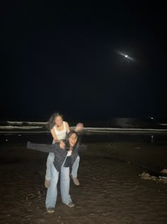 two women are standing on the beach at night with their arms around each other and one is holding another woman