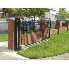 an iron fence and gate in front of a brick building with cars parked behind it