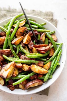 a white bowl filled with green beans and potatoes on top of a table next to a fork