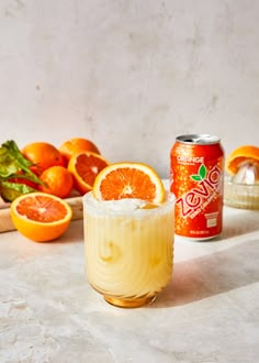 an orange drink is sitting next to some sliced oranges and other fruit on the table