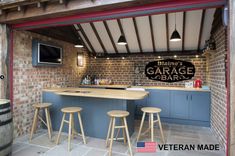 an outdoor kitchen area with bar stools and television mounted to the brick wall behind it