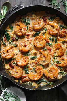 a skillet filled with shrimp and spinach on top of a wooden table next to utensils