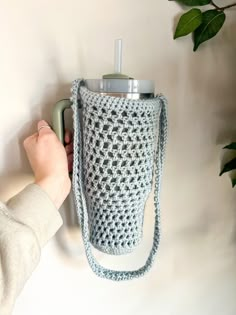 a person is holding onto a crocheted cup holder with a water bottle in it