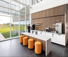 a coffee bar with orange stools in front of large windows