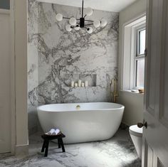 a white bath tub sitting next to a toilet in a bathroom under a chandelier