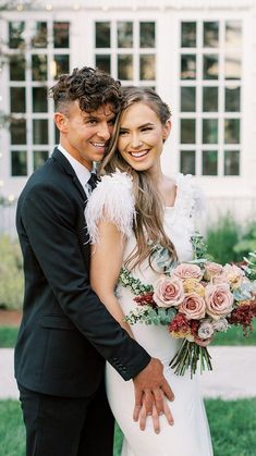 a bride and groom pose for a photo in front of a white building with large windows