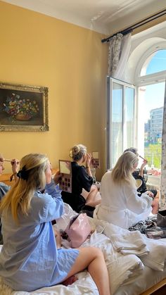 three women sitting on a bed in front of a window and looking out the window