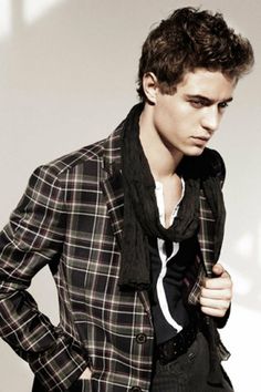 a young man is wearing a black and white plaid jacket with a scarf around his neck